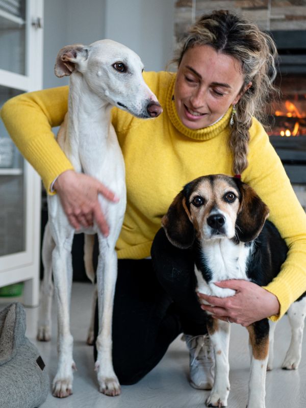 Woman gently holding and caring for two dogs inside a home.